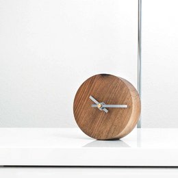 A minimalist table clock made of oak, walnut, or black walnut wood with a round, simple design.