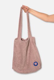 A large, soft, and plush pink beach bag or shopper made of fuzzy material with a circular logo patch on the front.