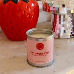  A scented candle in a pink container with a strawberry design, surrounded by a yellow and green tiled background.