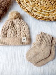 Beige merino wool baby slippers with a knitted texture and a bow detail.