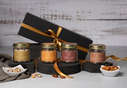 A gift box containing an assortment of gourmet nuts, including various flavors and textures. The box is wrapped in a black ribbon with a gold accent, creating an elegant and premium presentation.