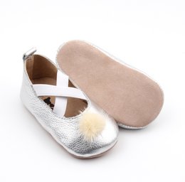 Silver leather ballet flats with criss-cross straps and white pom-pom accents, suitable for babies and toddlers.
