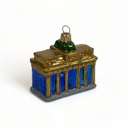 Ornamental glass figurine depicting the Brandenburg Gate, a famous landmark in Berlin, Germany. The figurine features a detailed gold-colored structure with blue accents, representing the iconic architecture of the gate.