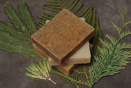 Handmade natural soap bars with banana and calendula extracts. Rectangular shape, earthy brown color, surrounded by green fern leaves.