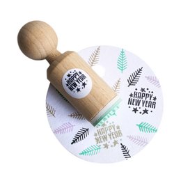 A small, round wooden stamp with the text "Happy New Year" and decorative elements like stars and leaves. The stamp is designed for creating festive holiday-themed impressions.