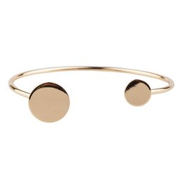 A gold-colored cuff bracelet with two circular discs on the ends.