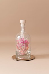 Dried pink flowers in a clear glass bottle with a cork lid. The bottle contains a decorative floral arrangement.