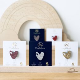 Glittering heart-shaped brooch in various metallic colors including silver, rose gold, gold, and multicolor. The brooch features a heart-shaped design with a sparkling, textured surface.