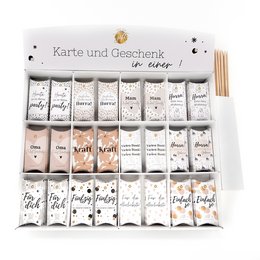 A display of 72 gift boxes in a German version, featuring a variety of tea-related designs and text. The boxes are arranged in a grid pattern and appear to be made of a light-colored material, possibly cardboard or paper. The overall design has a minimalist and monochromatic aesthetic.