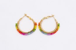 Stainless steel gold-tone earrings with a vibrant rainbow-colored crystal design. The earrings feature a hoop shape and a mix of colorful crystals that create a bold, statement-making look.