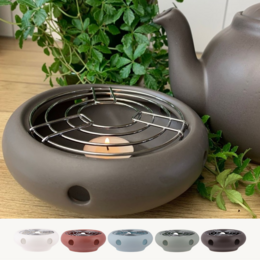Ceramic teapot heater with round shape and matte finish in various colors including white, terracotta rose, ice, leaf, and almost black.