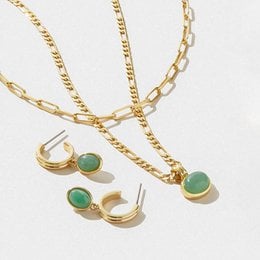Gold-toned necklace and earrings set with emerald-colored stones. The necklace features a delicate chain with a pendant, and the earrings have a simple stud design. This jewelry set has a classic and elegant style.