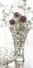 A tall, clear glass vase with a floral pattern featuring purple allium flowers and delicate greenery.