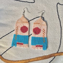  Handmade, statement earrings in a vibrant red, white, and blue color palette. The earrings feature a triangular shape with beaded fringe detailing, creating a bold and eye-catching accessory.
