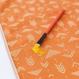 Orange splat mat with geometric arrow pattern, waterproof playmat for babies and toddlers.