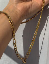 Gold-tone circular charm on a figaro chain necklace. Elegant and versatile accessory.