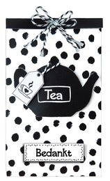 A black and white polka dot gift bag containing a tea bag and the text "Merci - 103 Thanks". The bag has a decorative bow on top.

The image shows a gift bag with a black and white polka dot pattern. The bag contains a tea bag and the text "Merci - 103 Thanks" is visible. The bag has a decorative bow on top, adding a festive touch.