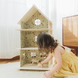 A large, multi-story wooden dollhouse with modern design elements. The dollhouse features multiple rooms and levels, providing ample space for imaginative play.