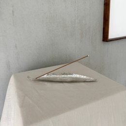 Silver-colored, leaf-shaped incense holder measuring 25 x 5 cm.