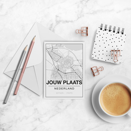 A6 card with a minimalist map design featuring the text "JOUW PLAATS NEDERLAND" (Your Place Netherlands). The card is surrounded by office supplies like pencils, a notebook, and a cup of coffee, creating a cozy workspace scene.