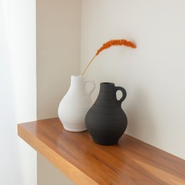 Two modern ceramic vases in black and white colors, displayed on a wooden shelf. The vases have a simple, minimalist design with a rounded, organic shape.