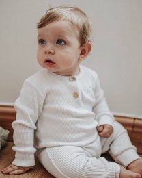 White ribbed baby romper with button closure, available in sizes 3-6 months to 12-18 months.