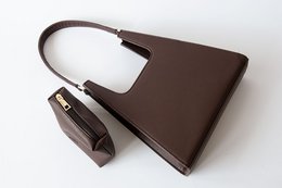 A brown leather handbag with a simple, minimalist design. The bag features a rectangular shape, a single strap, and a zipper closure.