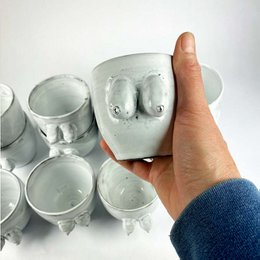 A handmade pottery mug with a unique boob-shaped design. The mug has a smooth, glossy finish in a light gray color.