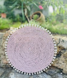 Round woven placemat in salmon color with decorative trim, suitable for dining table or home decor.