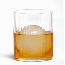 A tall, round glass tumbler with a ribbed design, filled with an amber-colored liquid, likely whiskey. The glass has a classic, elegant appearance suitable for serving premium spirits.