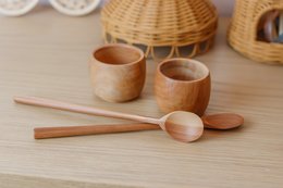 Two sustainable wooden tea cups with wooden spoons and utensils on a wooden surface.