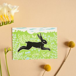 A green and white postcard featuring a silhouette of a running rabbit against a grassy background.