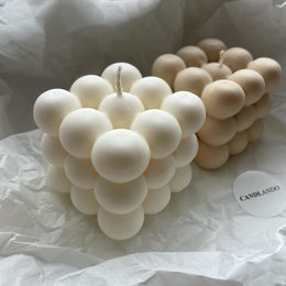Spherical, cream-colored wax candles in a cluster formation. The candles have a smooth, uniform texture and appear to be made of high-quality wax.