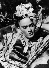 Frida Kahlo postcard featuring a black and white portrait of the artist with a floral headpiece, set against a colorful, patterned background.