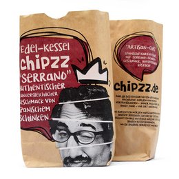 Serrano potato chips in a paper bag with an image of a man wearing glasses. The chips are described as "Edel-Kessel" which means "premium quality" in German.