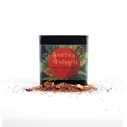 A festive green and red tin container holding a spiced holiday tea blend, with a cozy winter scene in the background.