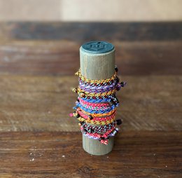  A wooden post with colorful bracelets displayed on it. The post is cylindrical in shape and has a light blue or gray finish. The bracelets are made of various materials and colors, including purple, pink, and blue threads or strings.