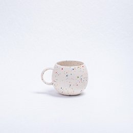 A round, white ceramic mug with a speckled pattern of colorful dots, suitable for parties and casual use.