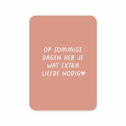 A greeting card with the text "Op sommige dagen heb je wat extra liefde nodig" (On some days you need a little extra love) in a handwritten-style font on a peach-colored background.