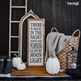 A rustic wooden sign with the text "There is magic in the night when the pumpkins glow by moon light" along with pumpkins, a basket, and other fall decor items.