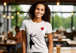  A white unisex t-shirt featuring the iconic Banksy artwork of a girl releasing a red heart-shaped balloon. The t-shirt has a simple, minimalist design that captures the essence of Banksy's street art style.