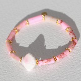 Pink beaded bracelet with gold accents, featuring a shell-shaped charm.