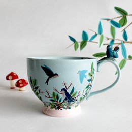 A colorful ceramic teacup featuring a whimsical garden scene with butterflies and flowers. The cup has a round, tall shape and is decorated with vibrant green leaves, red flowers, and black silhouettes of butterflies.