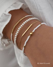 A set of delicate, stackable bracelets in bright white, gold, rose gold, and light silver colors. The bracelets feature a mix of beads, chains, and charms for a stylish and versatile look.