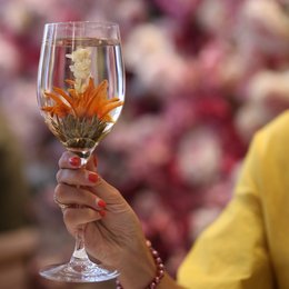 A clear glass wine glass with a floating flower inside, creating a beautiful and unique visual effect. The glass is set against a blurred background, adding to the artistic and elegant presentation.