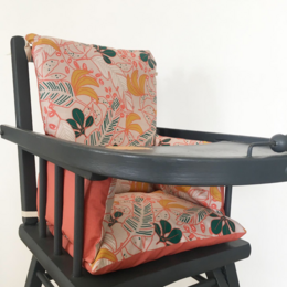 Colorful floral patterned cushion for a baby high chair, with a dark wooden frame and red fabric.