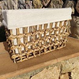  A large, rectangular storage basket made of woven natural materials, likely rattan or wicker, with a neutral-colored fabric lining. The basket has a structured, geometric design with a repeating pattern of interlocking shapes.