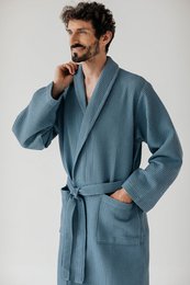 A long, light blue bathrobe made of a soft, waffle-knit material. The robe has a shawl collar, long sleeves, and a self-tie belt at the waist. It appears to be a comfortable and cozy option for lounging or after a bath.