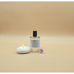 Floral, feminine perfume in a glass bottle with a black cap. The perfume is accompanied by a white candle and a pink flower, creating a serene and elegant display.