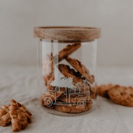 Glass storage jar with wooden lid, containing a miniature wooden car ornament. The jar is filled with holiday-themed cookies or snacks.